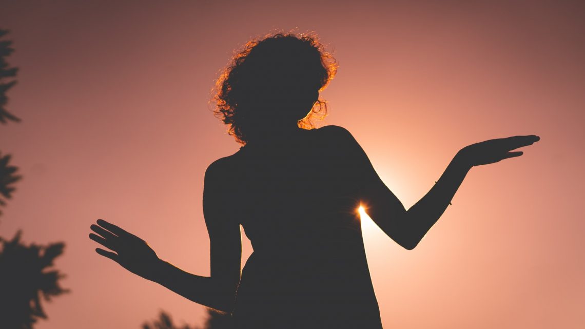 silhouette of woman raising her hands during sunset